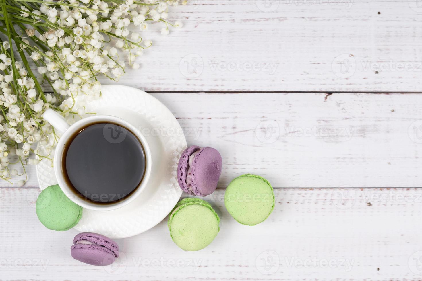 Colorful macaroons, a cup of coffee and lilies of the valley on wooden background, close-up flat lay. photo