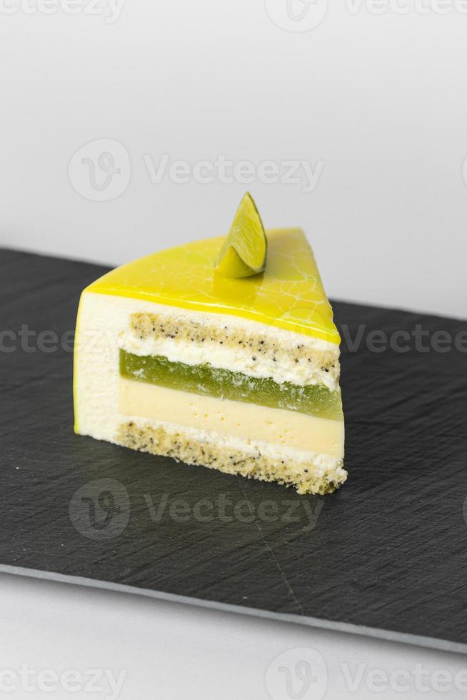 Close-up piece of mousse cake covered yellow mirror glaze with a slice of lime. French dessert photo