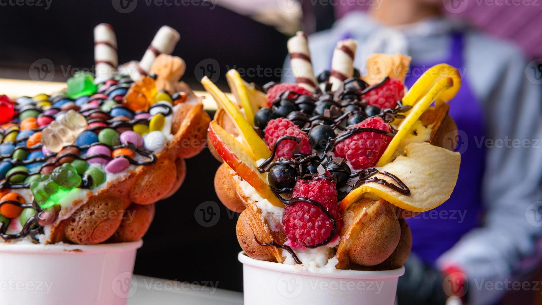 Bubble waffles with raspberries, chocolate and marshmallow in white paper cups are sold on Open kitchen food festival event. Hong kong waffles. photo