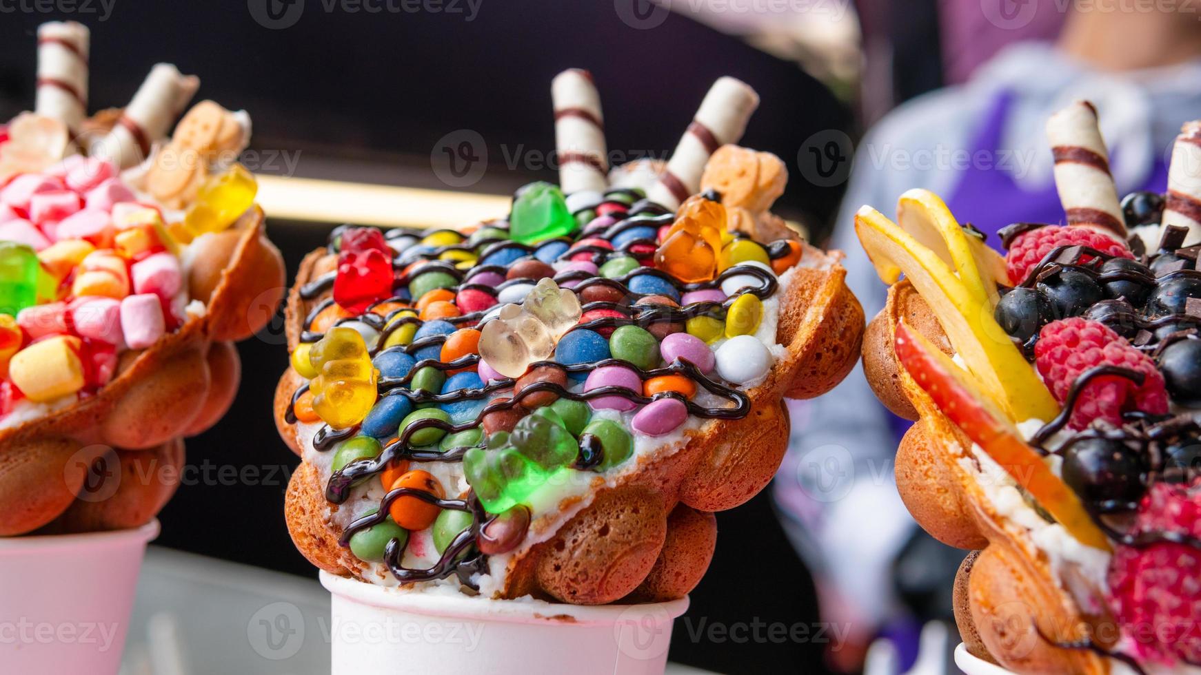 Bubble waffles with raspberries, chocolate and marshmallow in white paper cups are sold on Open kitchen food festival event. Hong kong waffles. photo