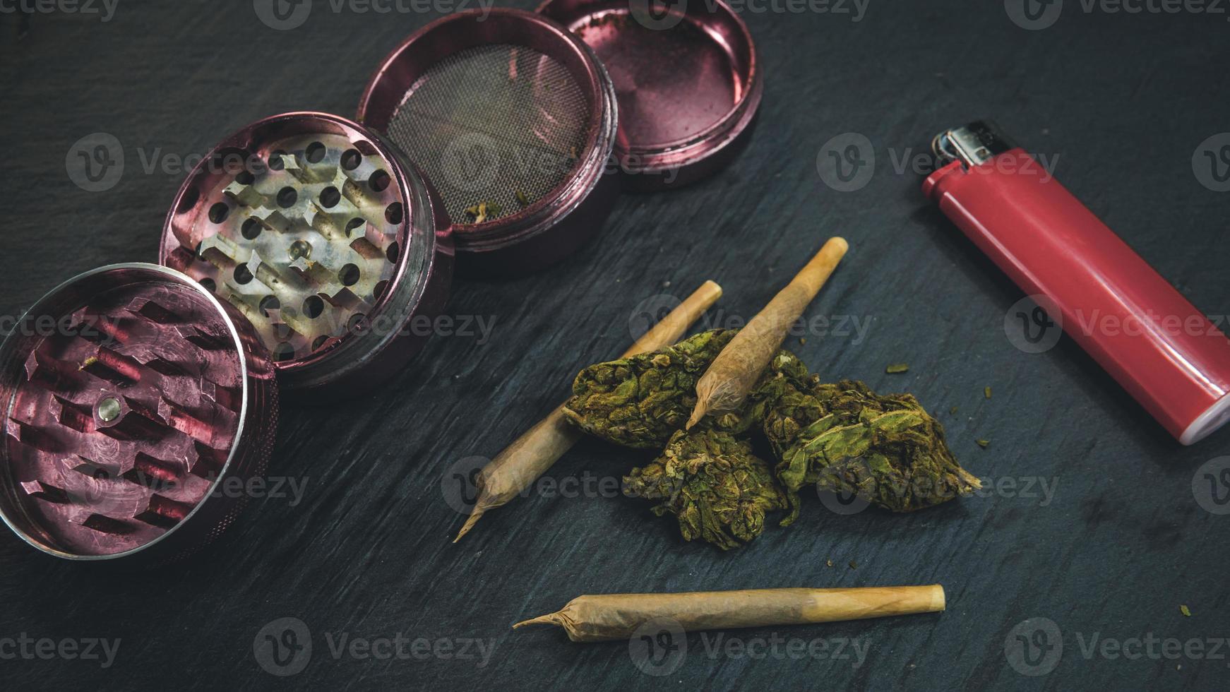 Marijuana buds and joint lie on a dark gray background. Grinder and lighter near cannabis photo