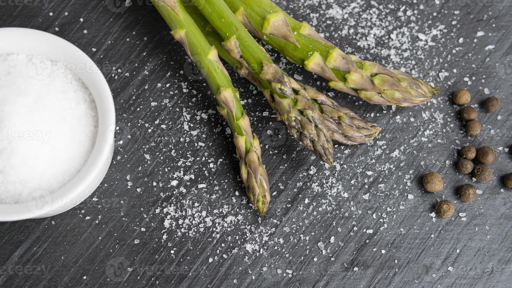 Close-up of organic fresh green asparagus with salt and pepper. Concept of  healthy vegetarian food, diet and home cooking. photo