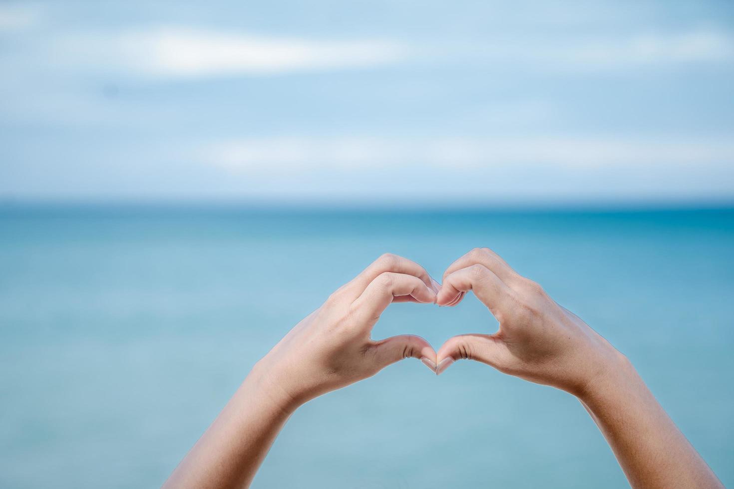Female hand in the shape of a heart against the sky, sea background, hands in the shape of a love heart. photo