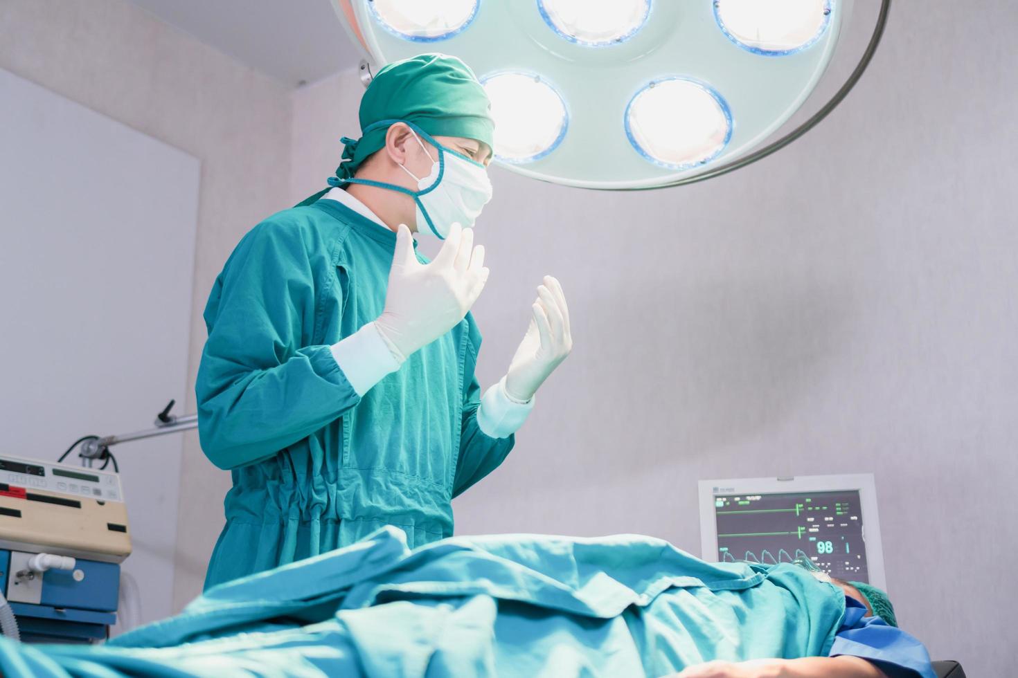 cirujano masculino con máscara quirúrgica en el quirófano del hospital, paciente en la cama con equipo médico que realiza una operación quirúrgica en el quirófano foto