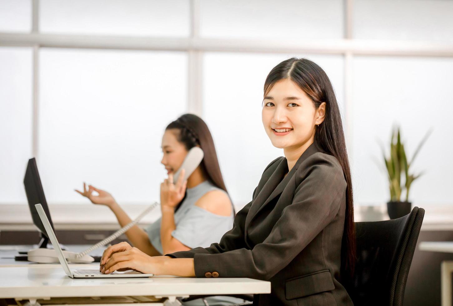 Smiling asian officer woman relax in office and looking at camera, young business woman sitting at desk, business people in office photo