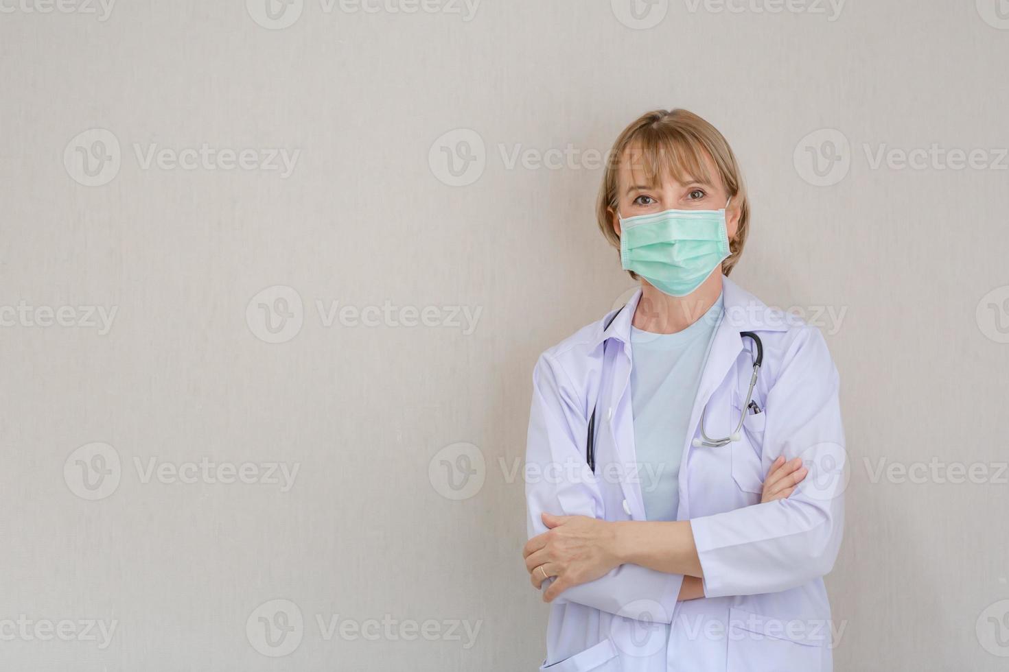 los médicos miran la cámara y sonríen mientras están de pie con los brazos cruzados en el hospital, una doctora con mascarilla protectora de pie con los brazos cruzados foto