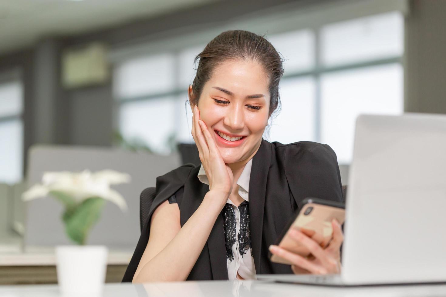 alegre empresaria usando el teléfono en la oficina. chica guapa emocionada que usa un teléfono inteligente en la oficina, mujer que trabaja en su oficina en casa foto