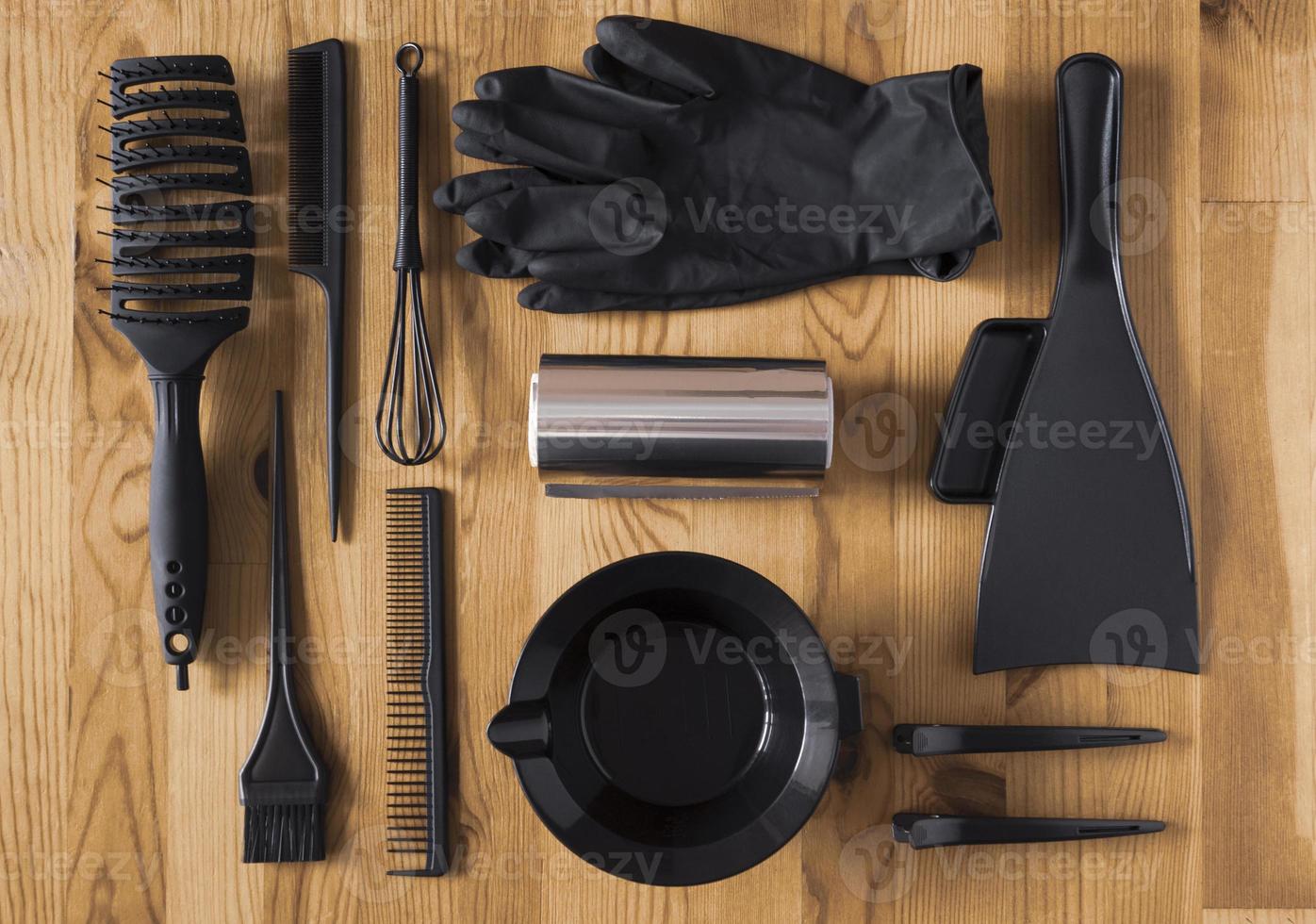 accesorios de color negro para teñir el cabello en una mesa de madera. cuenco, cepillo, peine, lámina y otros accesorios de peluquería, vista superior. foto