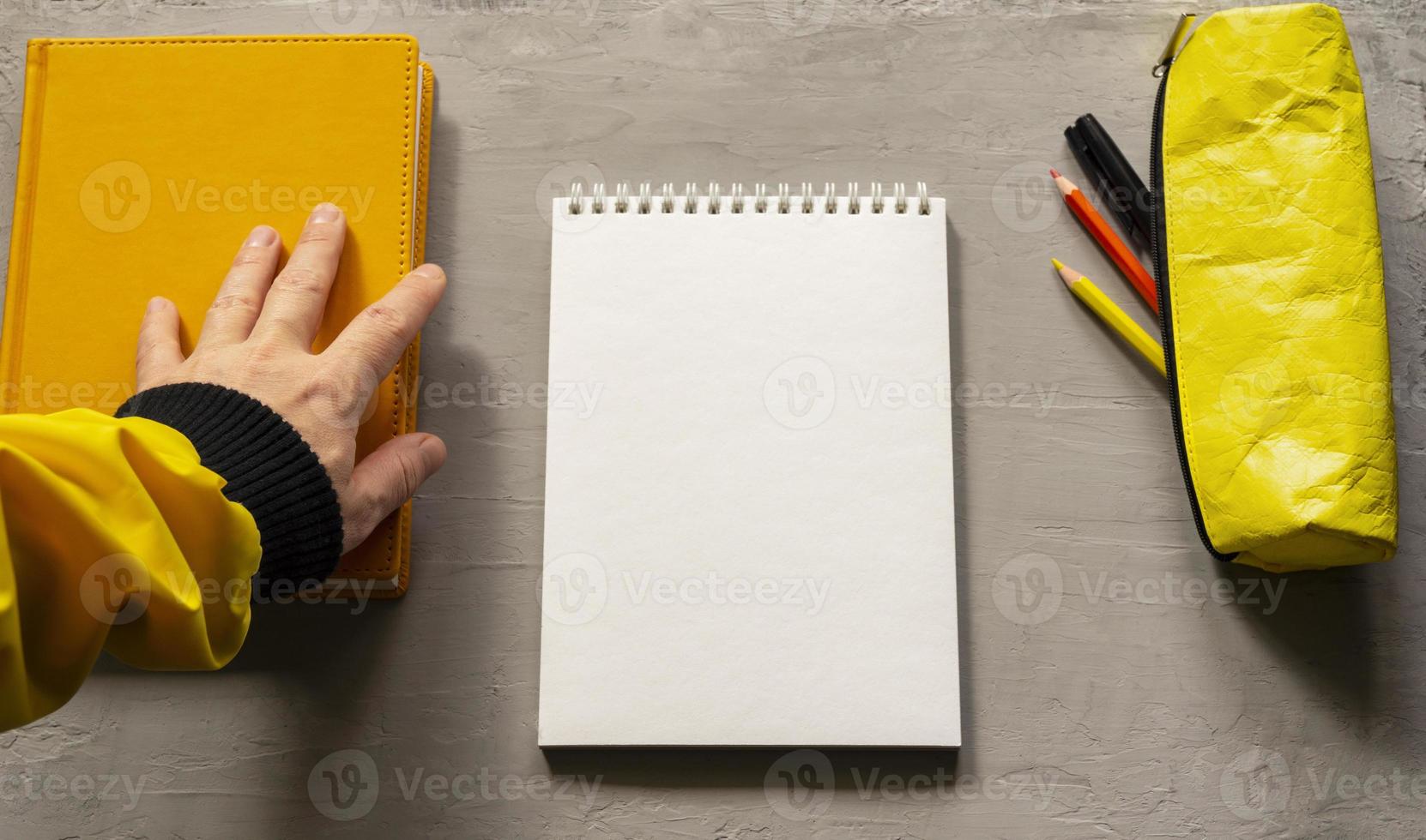 An empty white notebook, a book, and a yellow pencil case. Top view of objects. photo