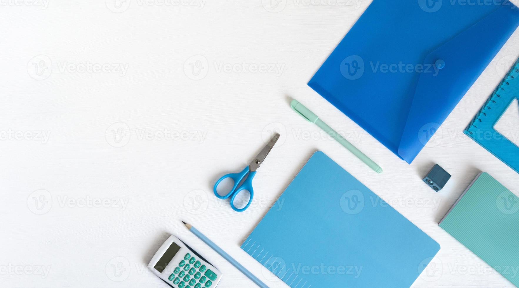 Blue green stationery in the corner and copy space. Accessories for writing and counting on a white table, a notebook, a ruler, scissors, a pencil, a pen. photo