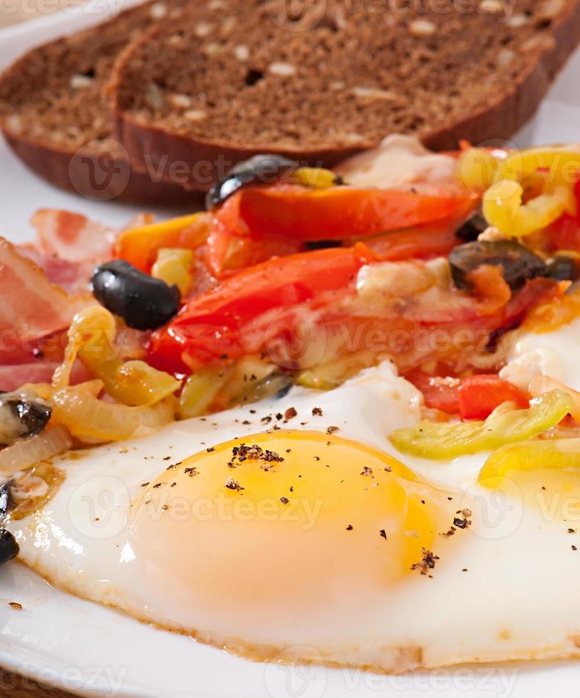 Breakfast - fried eggs with bacon, tomatoes, olives and slices of cheese photo