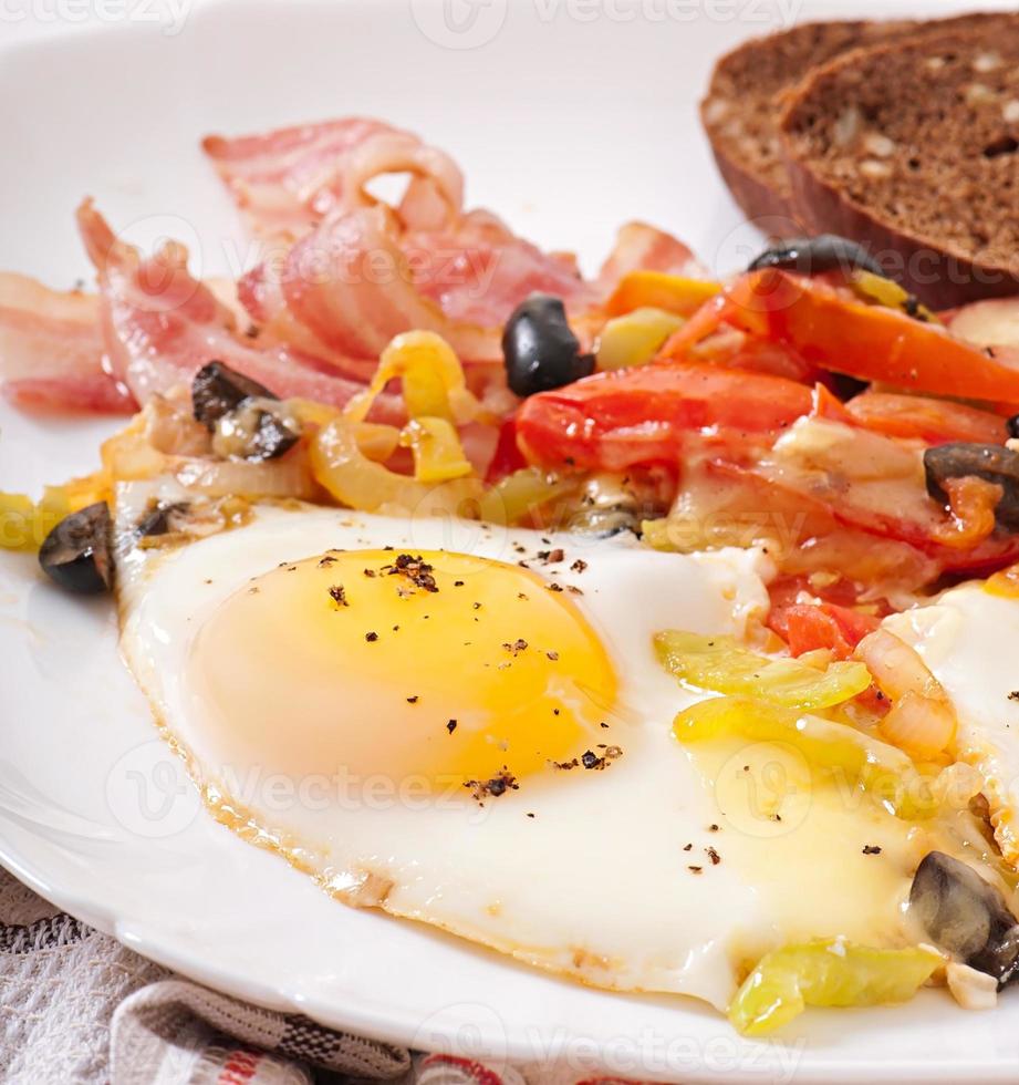 Breakfast - fried eggs with bacon, tomatoes, olives and slices of cheese photo