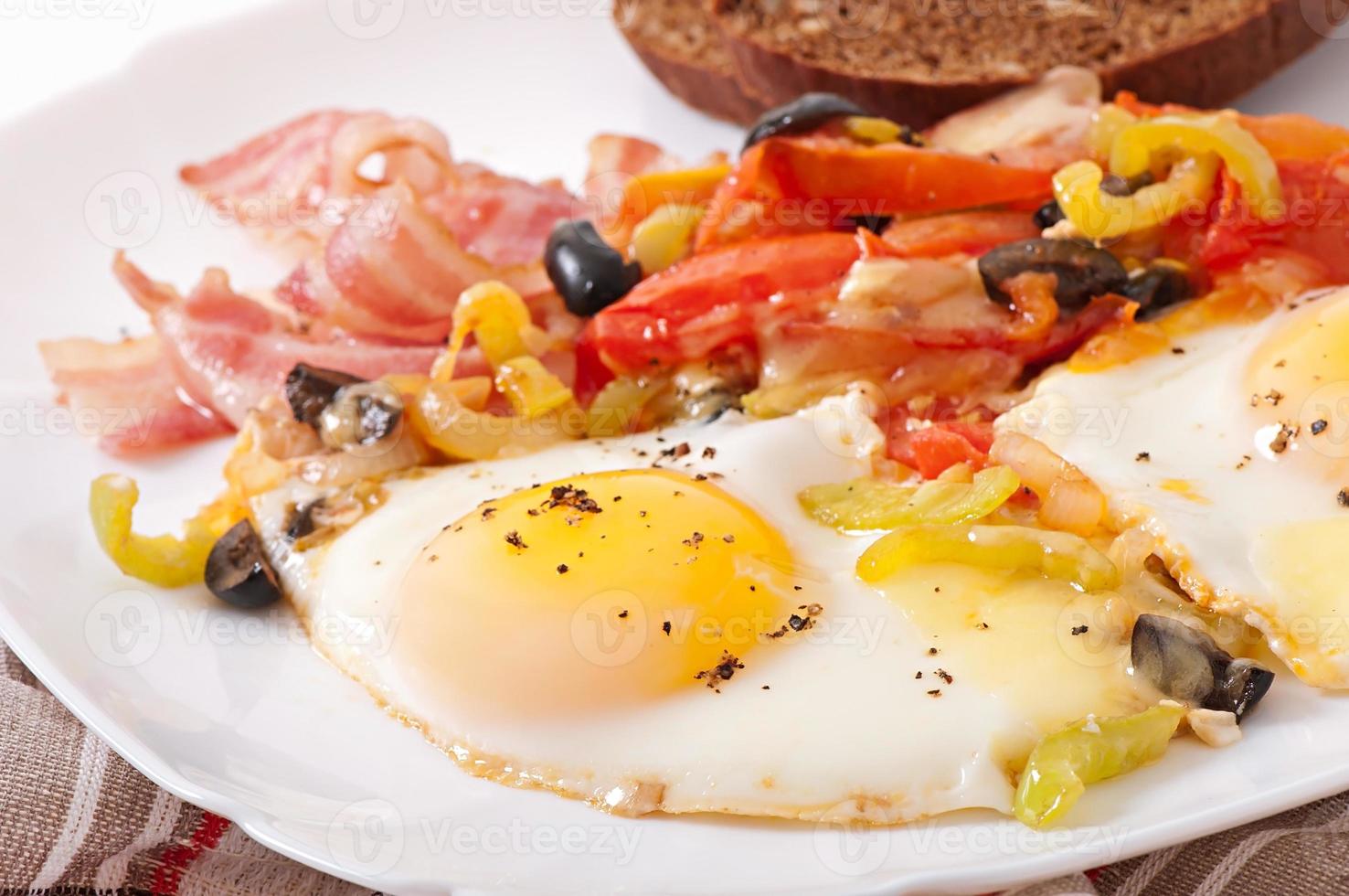 Breakfast - fried eggs with bacon, tomatoes, olives and slices of cheese photo