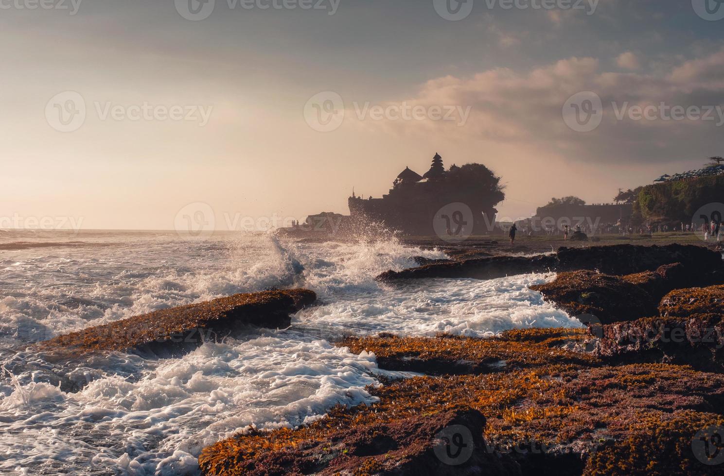 Pura Tanah Lot temple on clifftop and wave hitting on sunset beach in Bali photo