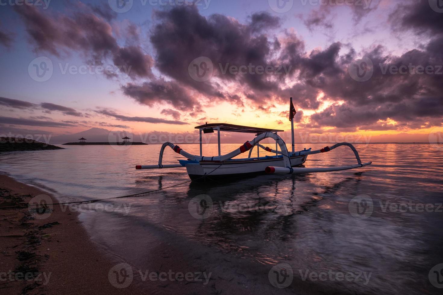 Ancient traditional Jukung fishing boat on seashore at colorful sunrise photo