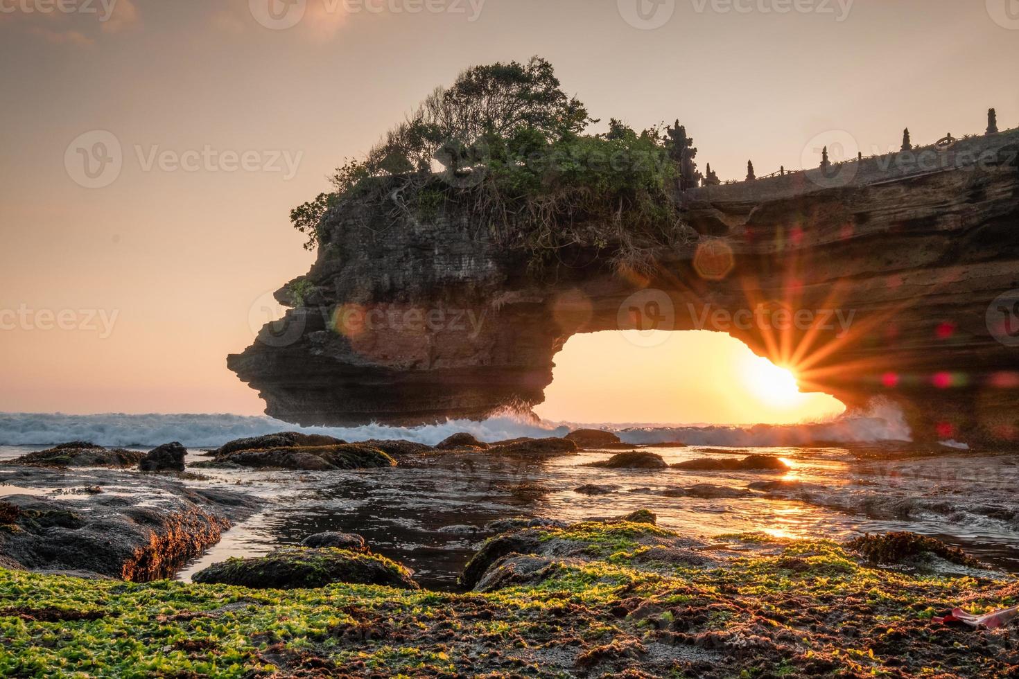 Sunshine through of rocky cliff on seashore at sunset photo