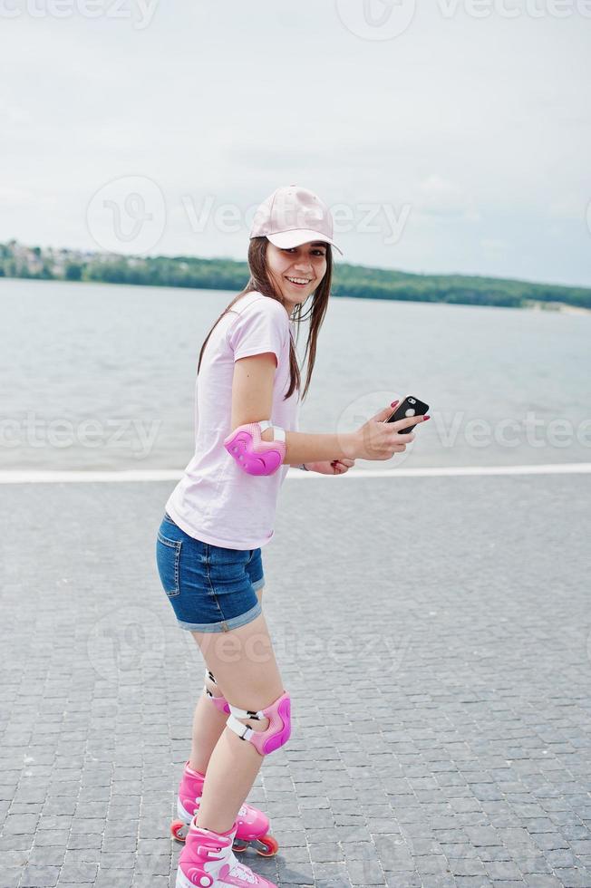 retrato de una fantástica joven patinando con su teléfono en las manos en el parque al lado del lago. foto