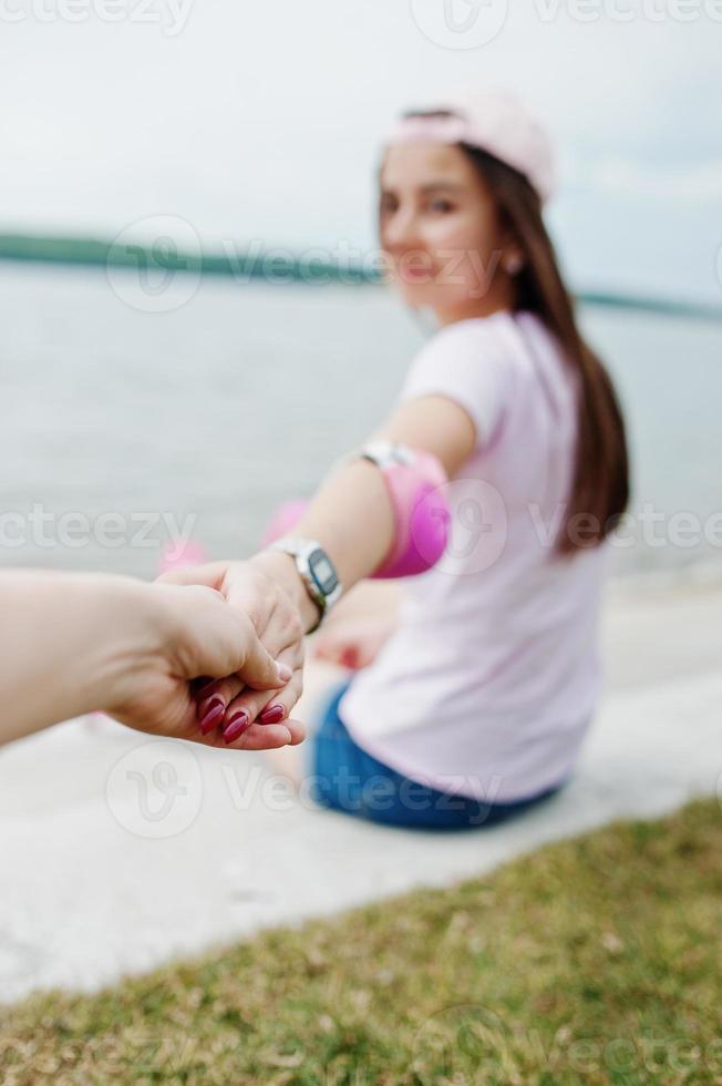 Close-up photo of couple holding hands while sitting on the ground next to the lake.