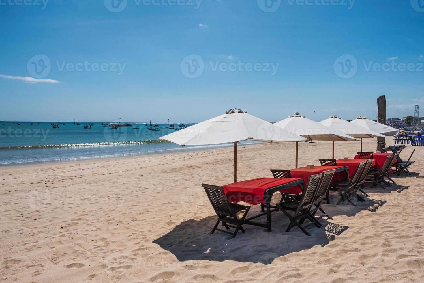 Red wooden dining table with white umbrella on the beach photo