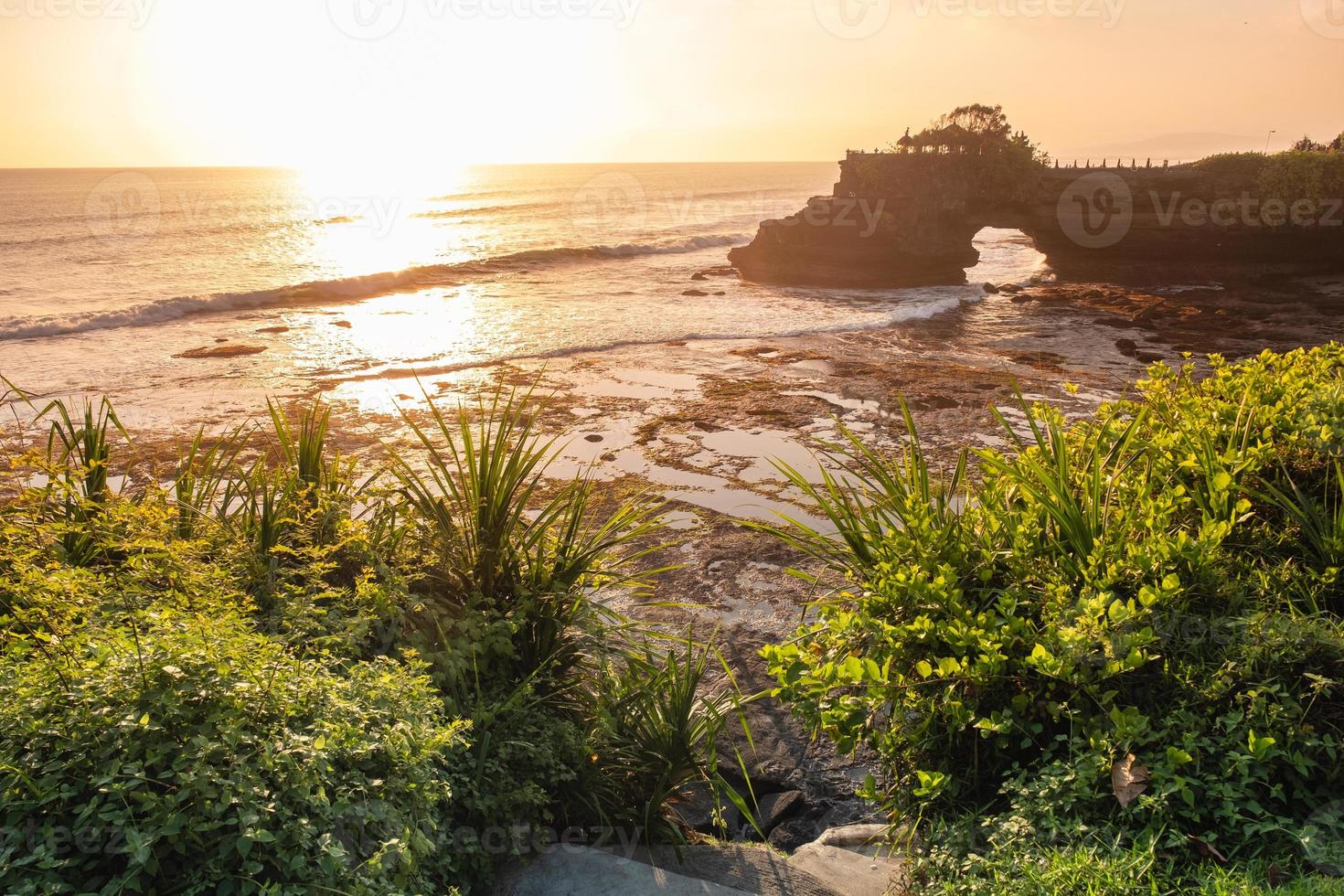 Pura Batu Bolong temple on rock cliff with tree on coastline at sunset photo