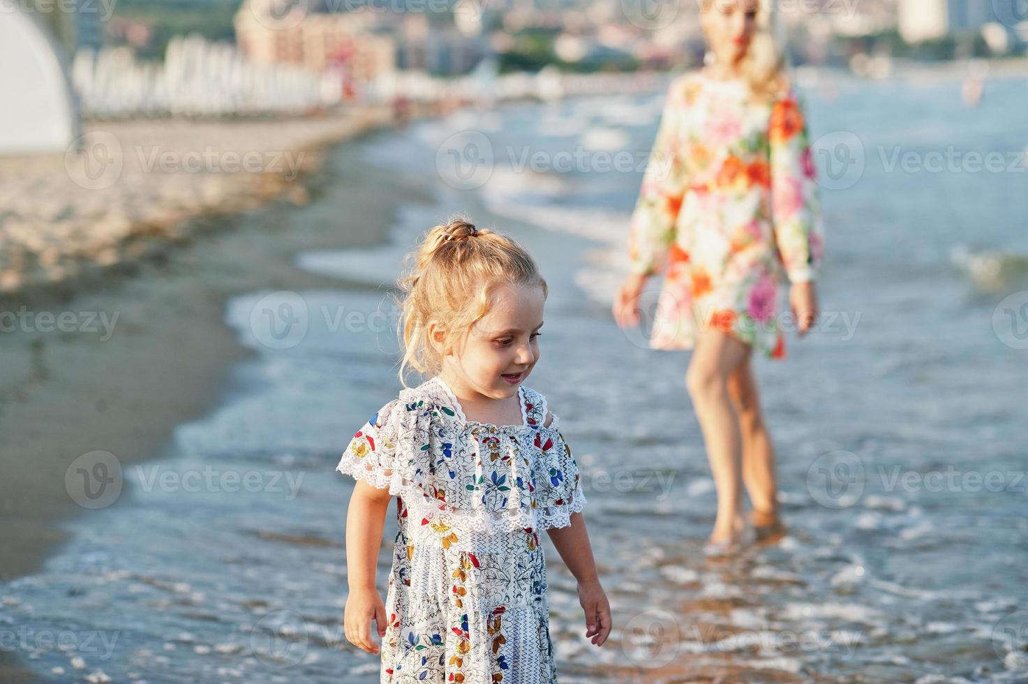 Mother and beautiful daughter having fun on the beach. Portrait of happy woman with cute little girl on vacation. photo