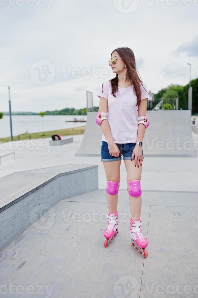 retrato de una mujer joven hermosa en pantalones cortos, camiseta y gafas de sol de pie al aire libre en patines. foto