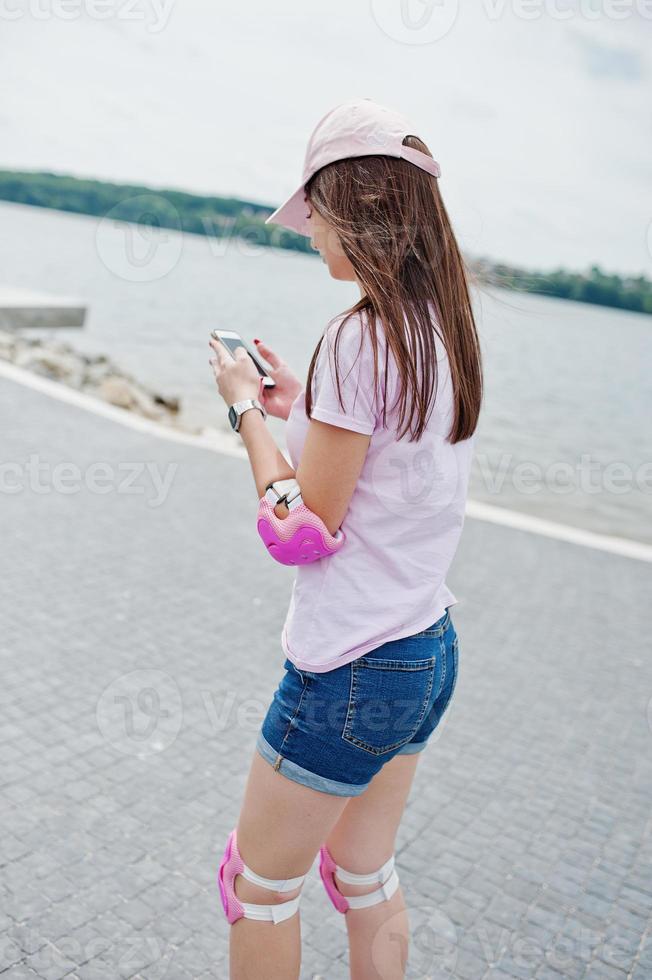 Portrait of a fantastic young woman roller skating with her phone in her hands in the park next to the lake. photo