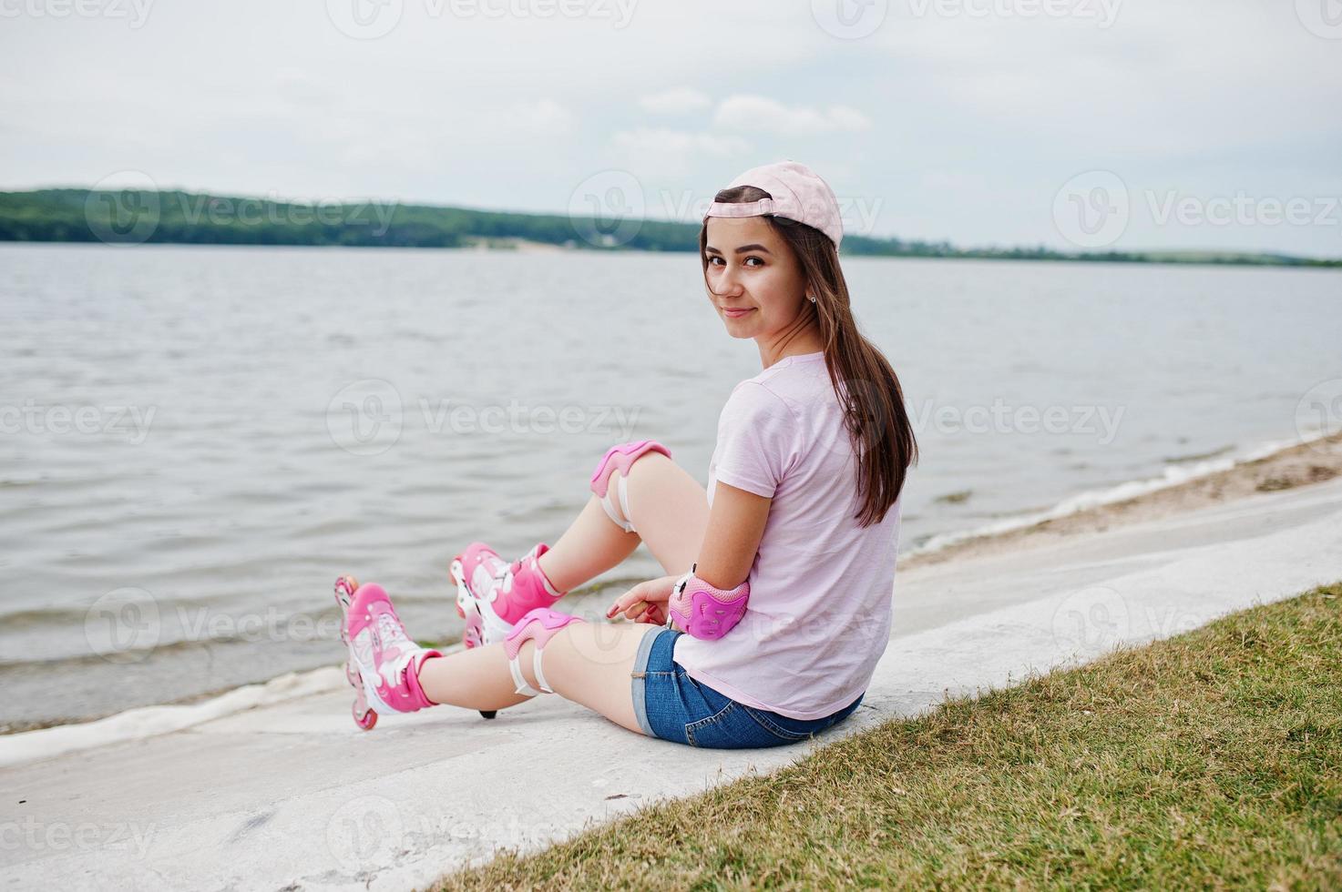 Portrait of a gorgeous young woman in casual clothes and cap sitting on the ground next to the lake. photo