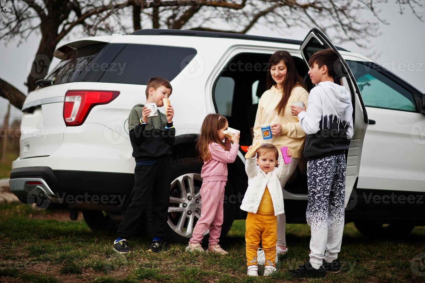 Mother with kids drink tea outdoor near white suv car. photo