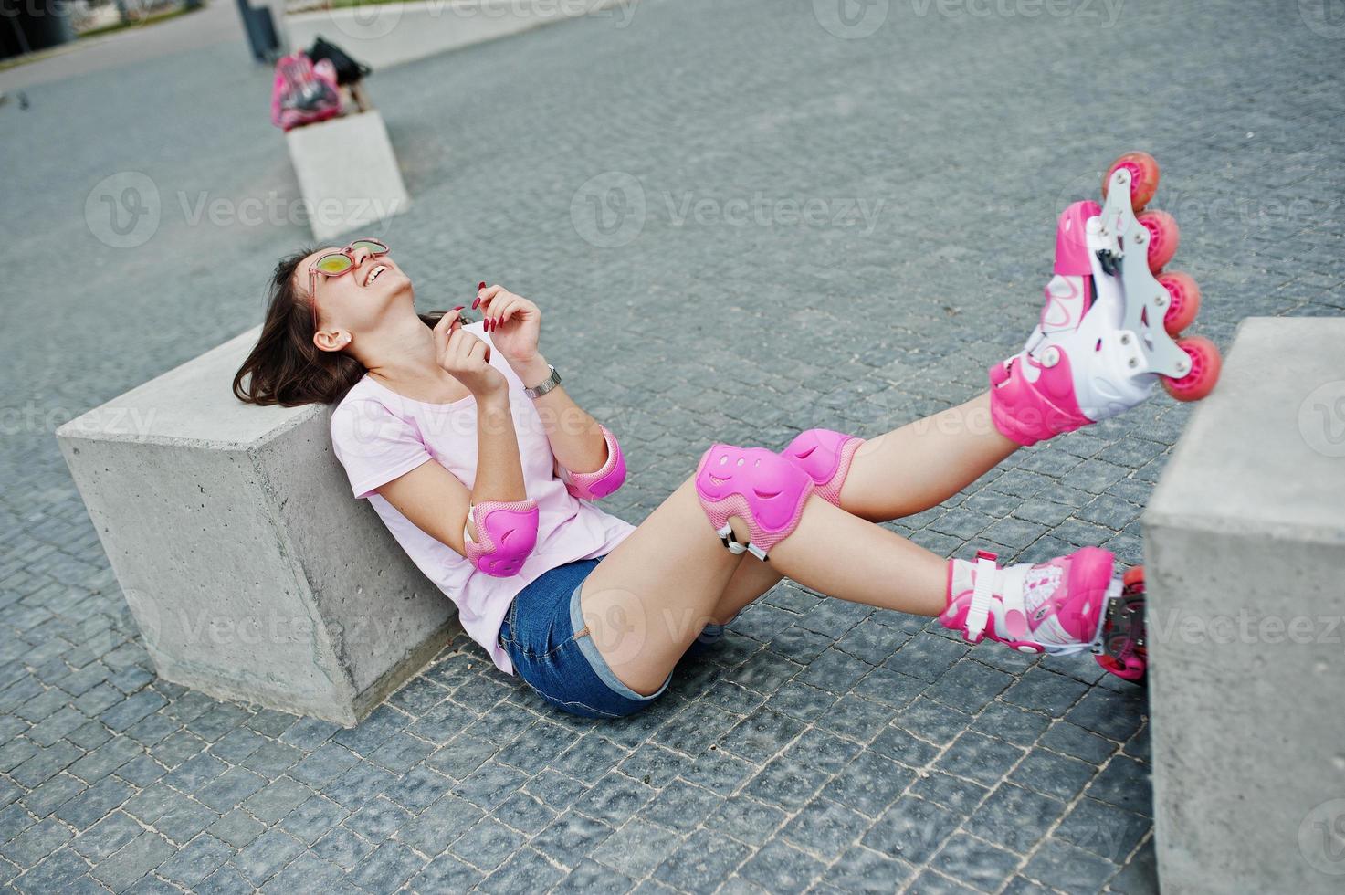 Portrait of a beautiful woman sitting on the ground next to concrete cube wearing rollerblades and casual clothes. photo