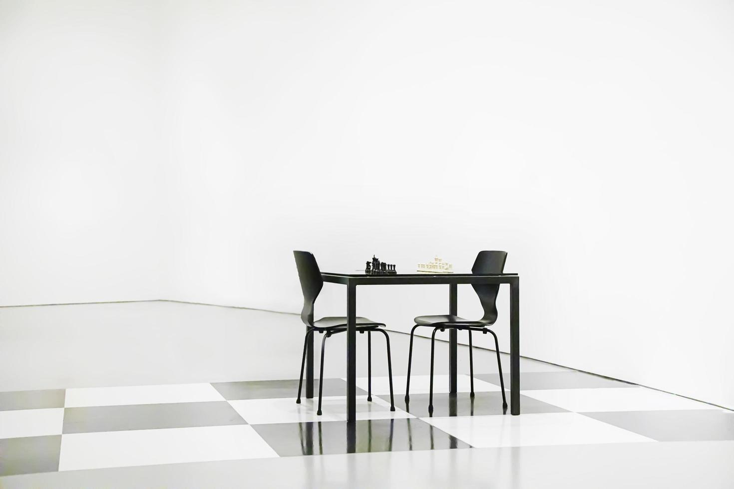 Black table and chairs with a chess board in a white room photo