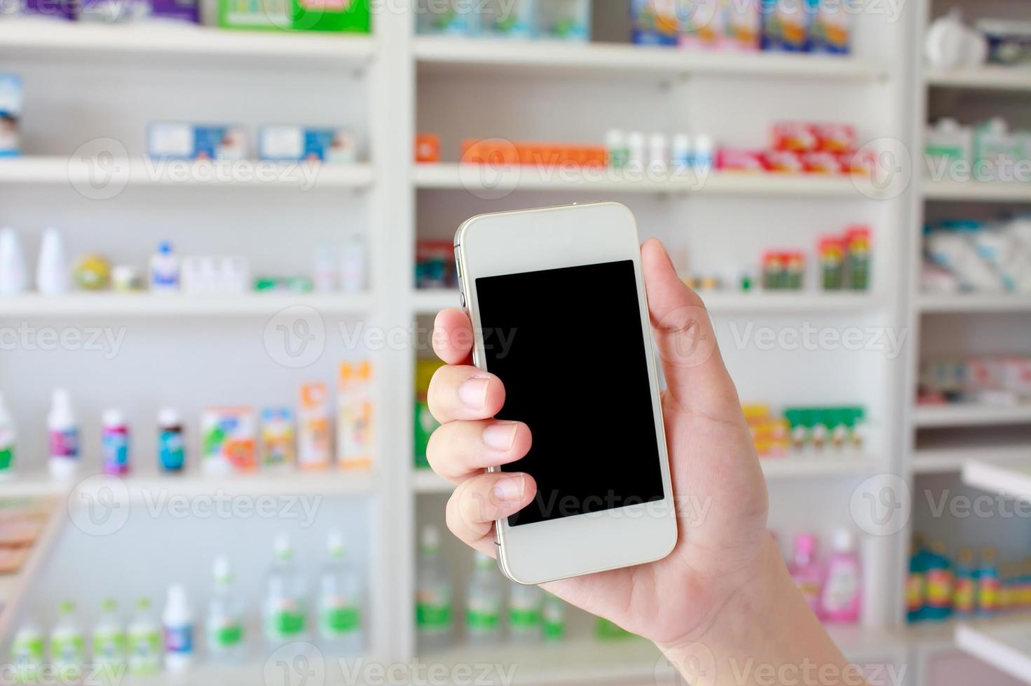 mano que sostiene el teléfono inteligente en la farmacia foto