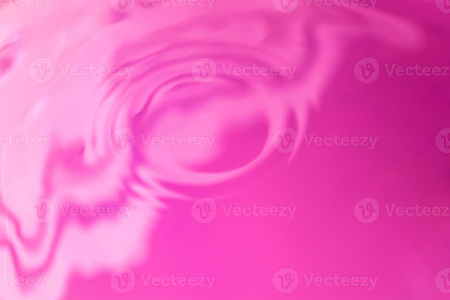 Fluid bright background. Texture of rose water with ripples, waves and circles. Close-up with light reflection. photo