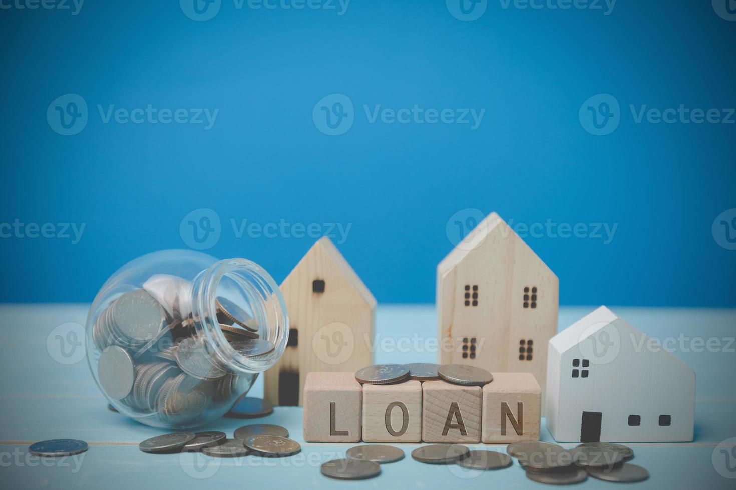 Text LOAN on wood blocks with coins. Behind have a little wooden house all on a blue desk. Financial, Investment estate, Loan, bank Concept. photo