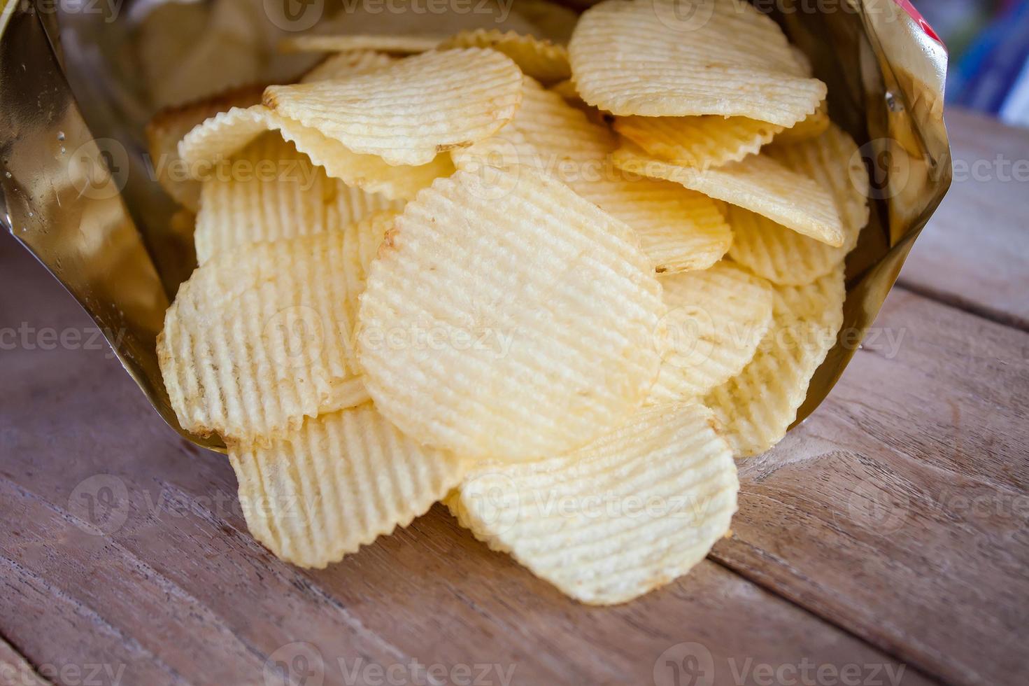 Opened pack with potato chips over wooden table photo