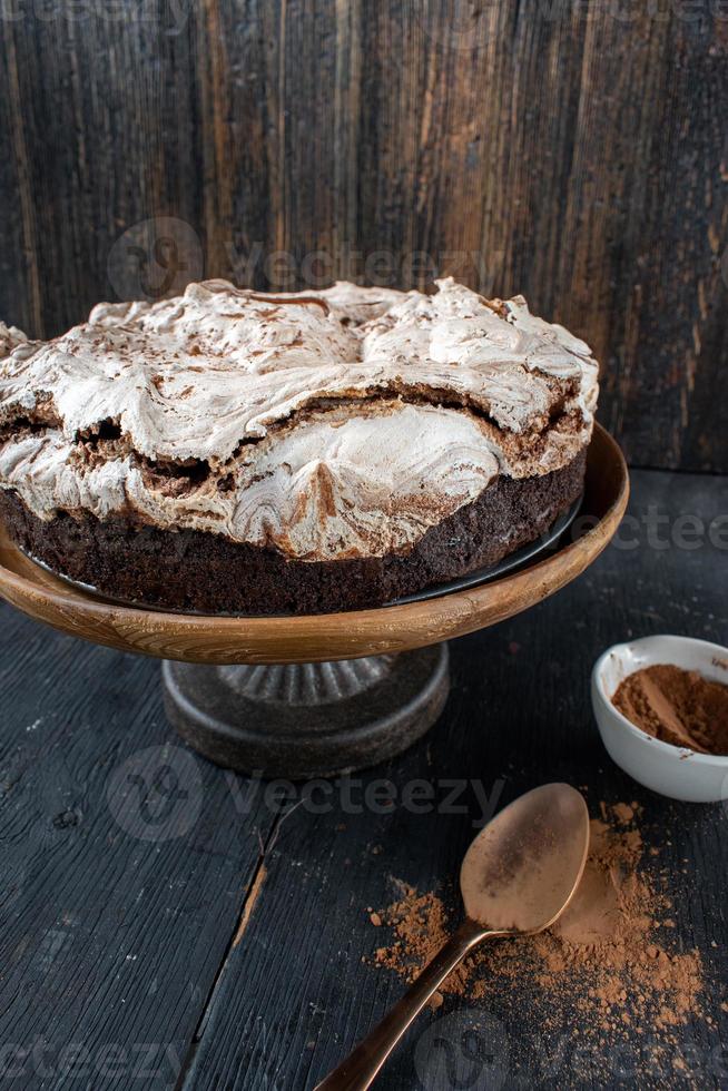 pastel de brownie horneado redondo cubierto con merengue y remolinos de chocolate en un soporte de pastel rústico foto