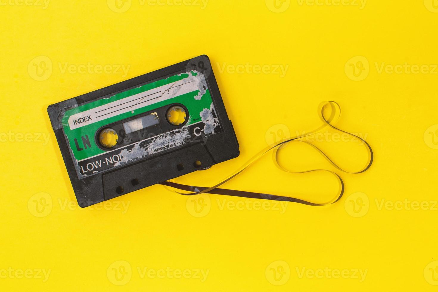 old retro cassette tape with grunge label surrounded by pulled tape pile on yellow background flat lay photo