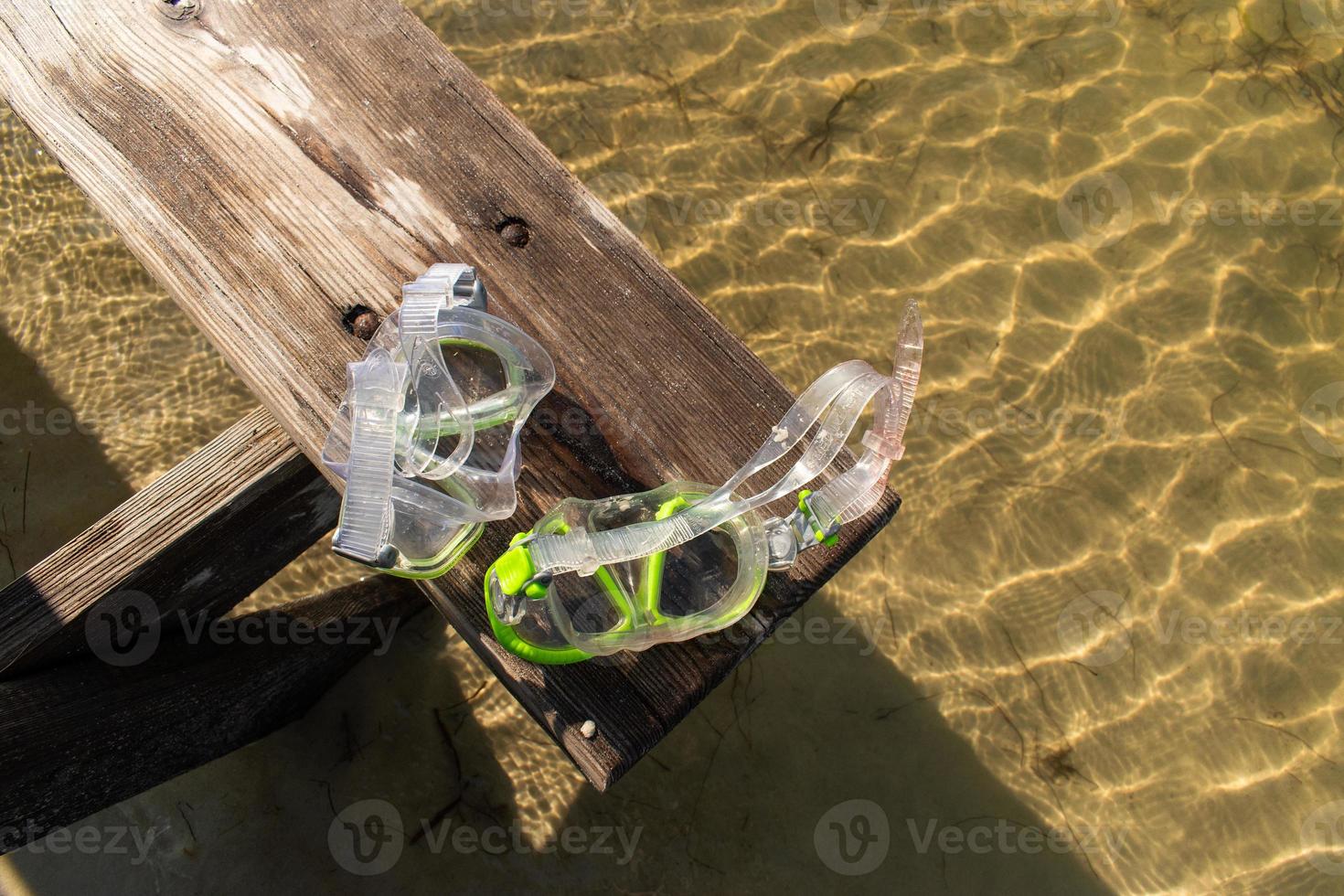 sun washed bench with diving goggles over bay water in sunlight photo