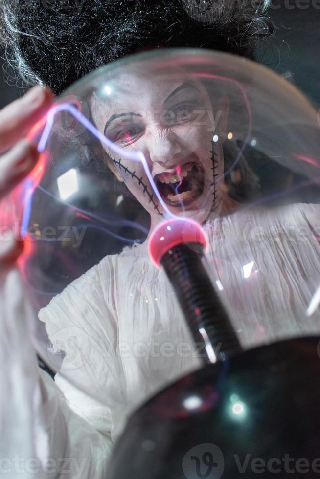 studio shot portrait of young girl in costume dressed as a Halloween, cosplay of scary bride of Frankenstein posing with glass lightning ball photo