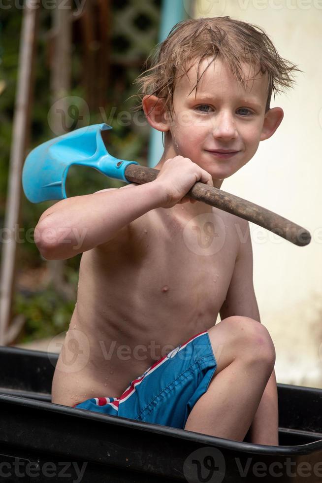 young boy playing in mud in wheelbarrow with shovel filled with water photo