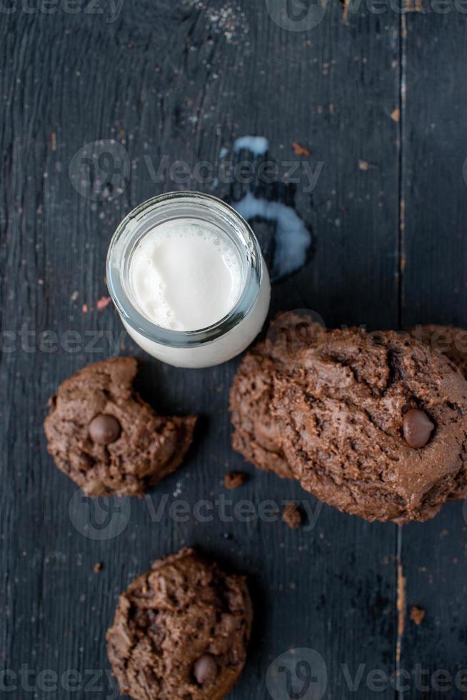 stack of chocolate chip cookies with milk on rustic wood table photo