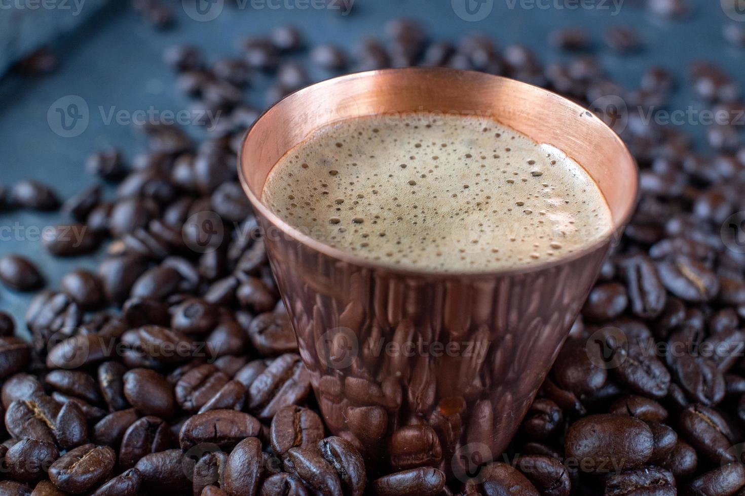 taza de cobre llena de café expreso en el centro de granos de café crudos esparcidos sobre una mesa rústica foto