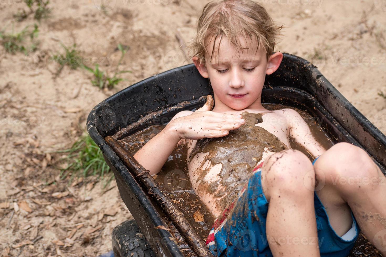 young boy playing in mud in wheelbarrow filled with water photo