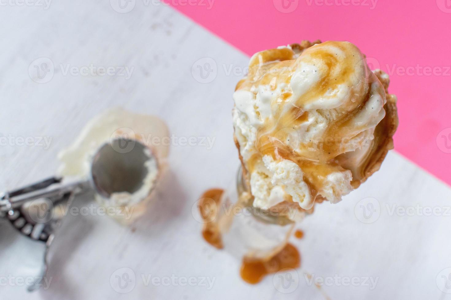 melting vanilla ice cream scoops with dripping caramel sauce over waffle cone on fun vibrant pink background photo