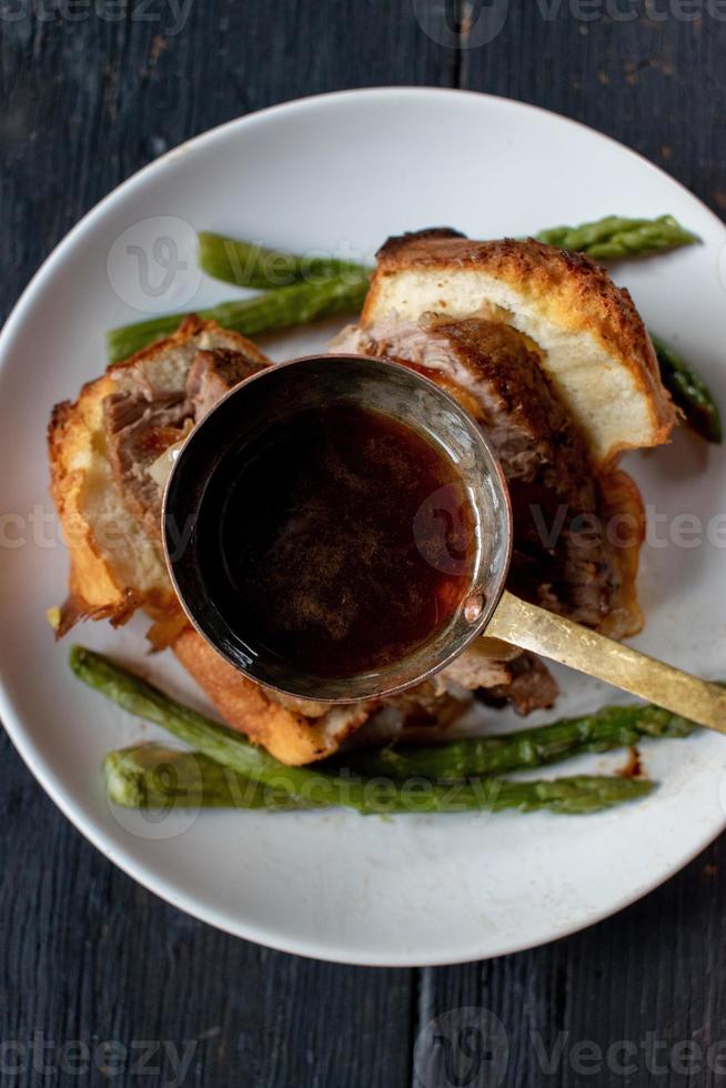 cucharón de salsa con caldo de res sobre pudín de yorkshire con res y espárragos foto