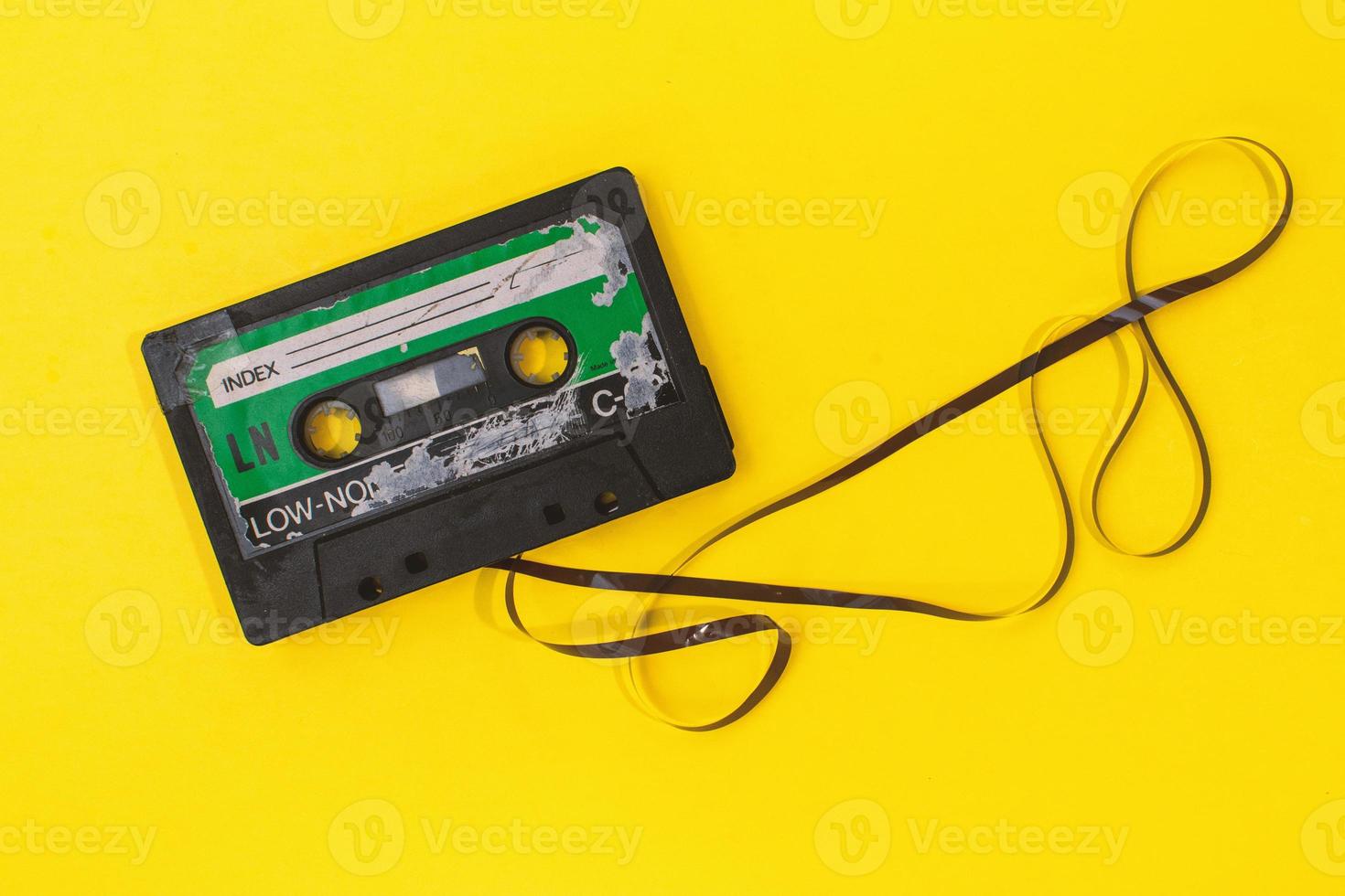 old retro cassette tape with grunge label surrounded by pulled tape pile on yellow background flat lay photo