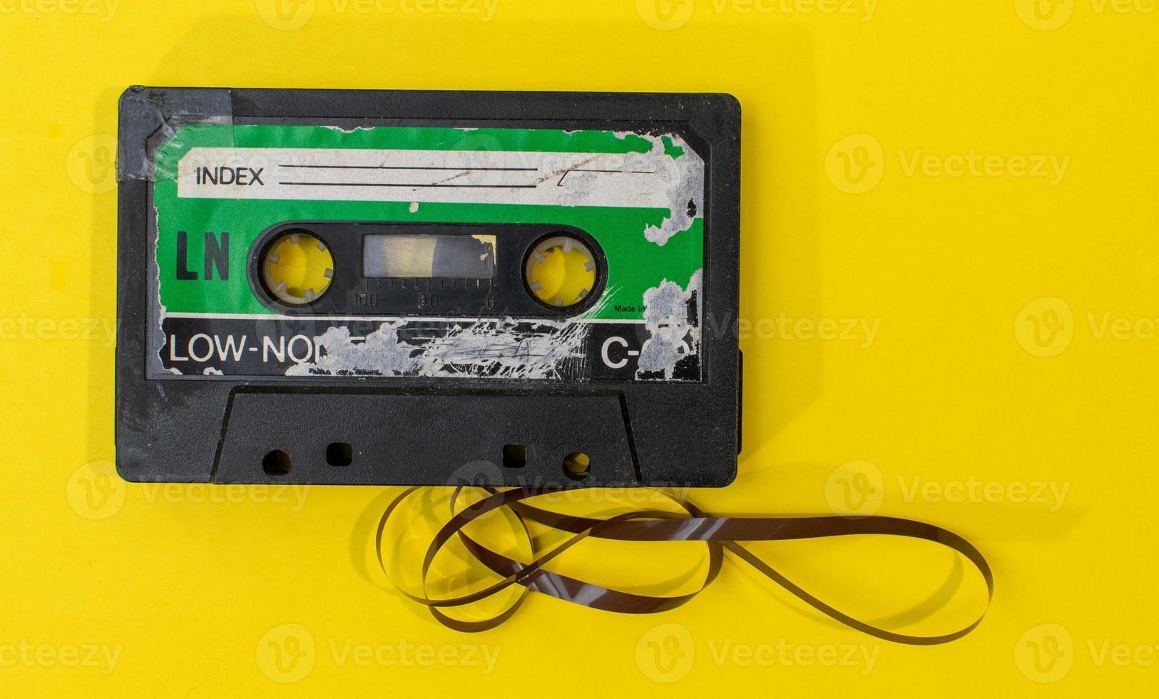 old retro cassette tape with grunge label surrounded by pulled tape pile on yellow background flat lay photo