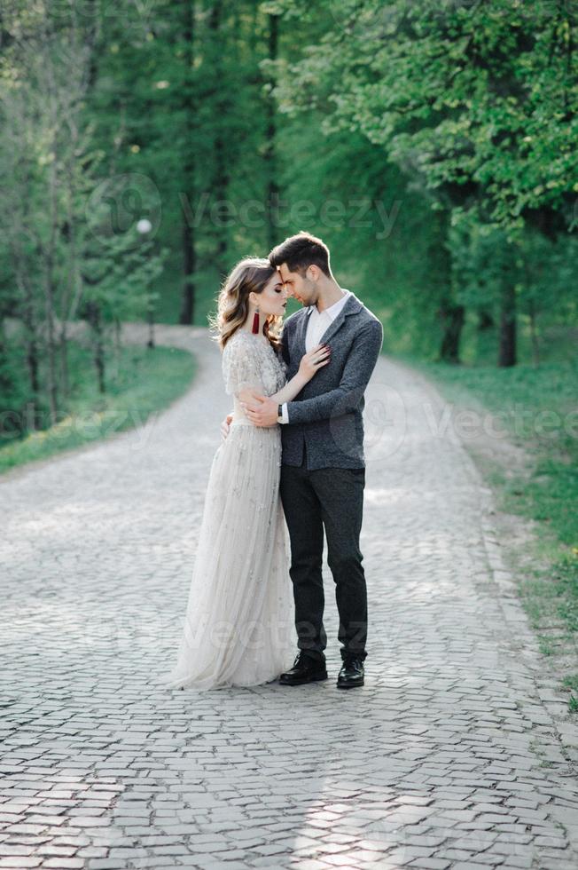 pareja vestida de boda con un ramo de flores y vegetación está en las manos contra el telón de fondo del campo al atardecer, la novia y el novio foto