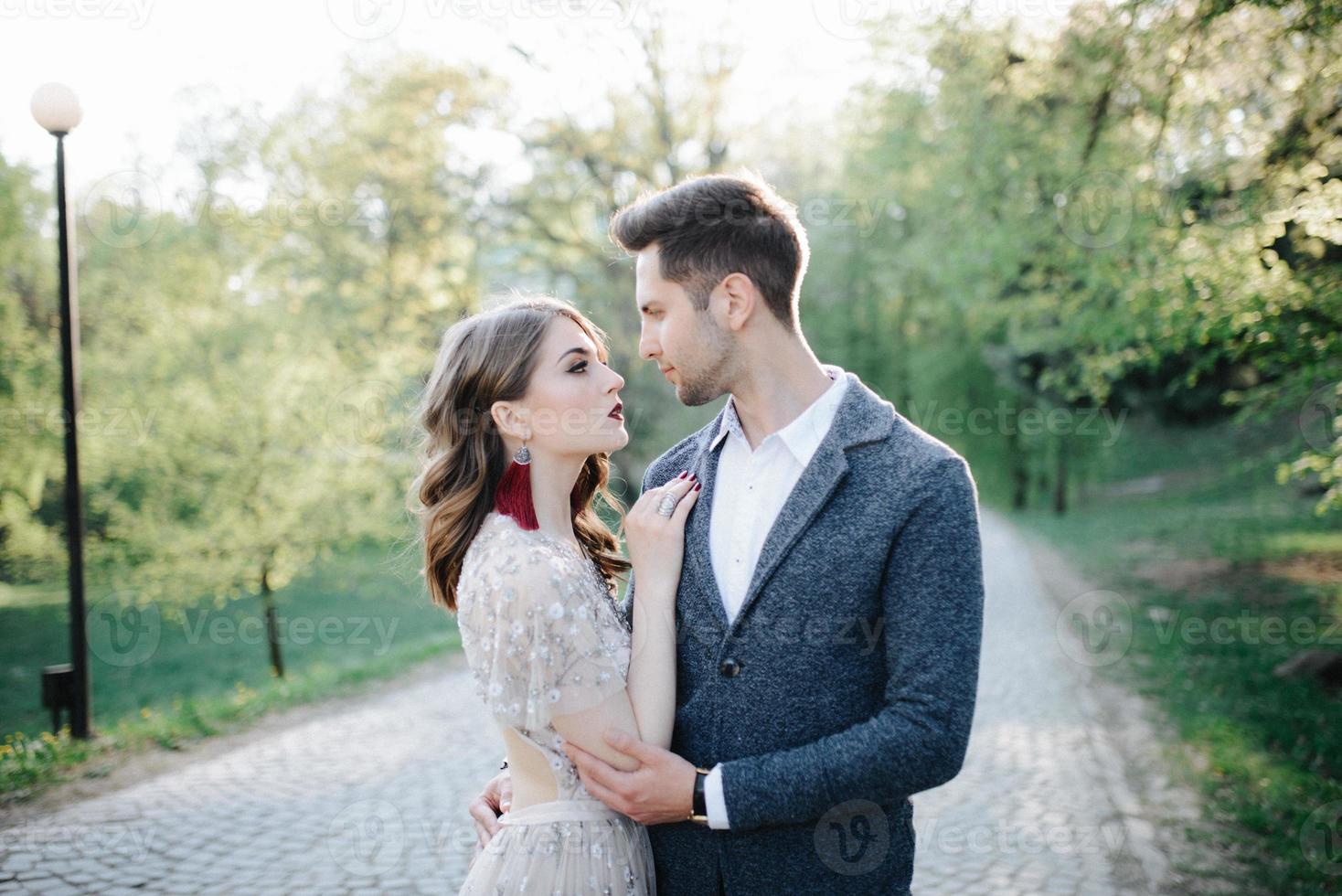 pareja vestida de boda con un ramo de flores y vegetación está en las manos contra el telón de fondo del campo al atardecer, la novia y el novio foto