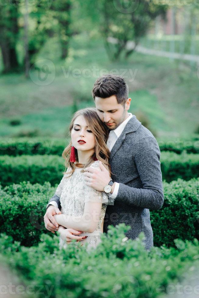 pareja vestida de boda con un ramo de flores y vegetación está en las manos contra el telón de fondo del campo al atardecer, la novia y el novio foto